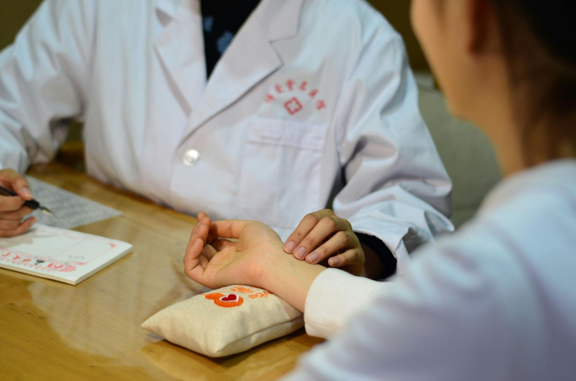 A doctor in a white coat is actively performing a one-on-one patient examination by checking their wrist and taking notes, an action that represents the detailed consultation at the best HIV PEP clinics in Singapore.